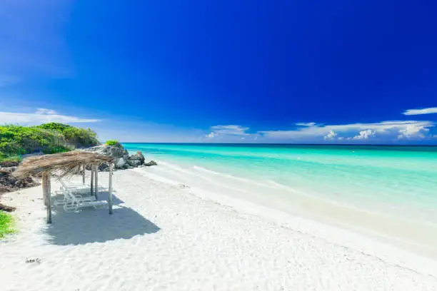 Photo of inviting view of tropical white sand beach and tranquil turquoise ocean on dark deep, blue sky background