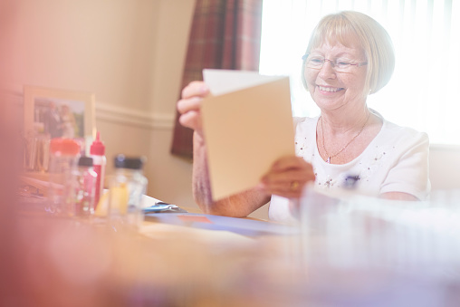 A senior woman sat at table making greetings cards