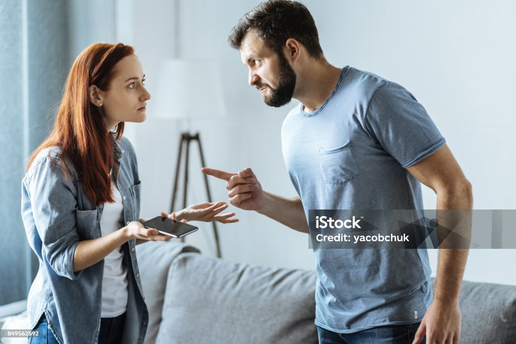 Angry upset man pointing at his wife Its your fault. Angry upset unhappy man looking at his wife and pointing at her while blaming everything on her Arguing Stock Photo