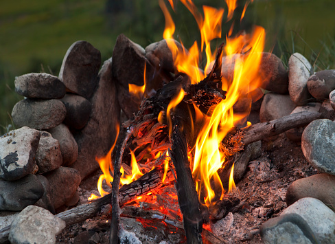Close up shot of a burning campfire with a stone fire circle in summer.