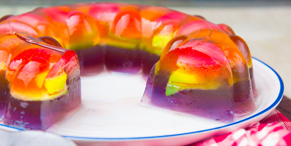 Colorful rainbow jelly on transparent plate with sugar milk white sauce