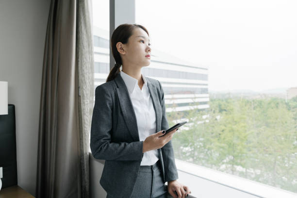 istock woman standing by window holding smartphone 849598792