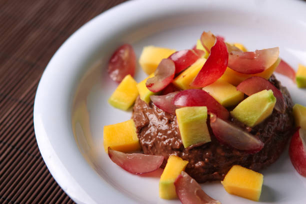 Chocolate pudding with mango and grape on white plate on wooden background