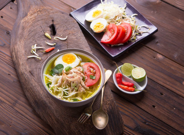 istock Soto: Indonesian chicken soup with hard boiled eggs, tomato, bean sprout, lemon, cayenne pepper on rustic brown wooden background 849604138