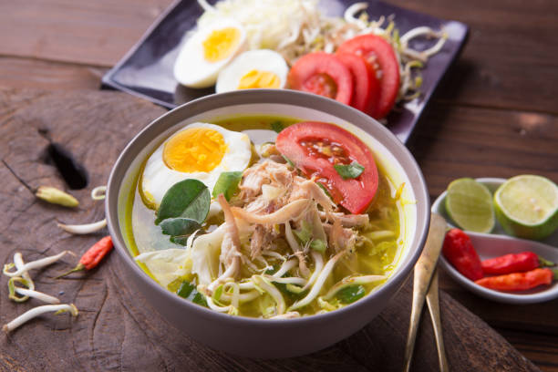 istock Soto: Indonesian chicken soup with hard boiled eggs, tomato, bean sprout, lemon, cayenne pepper on rustic brown wooden background 849604154