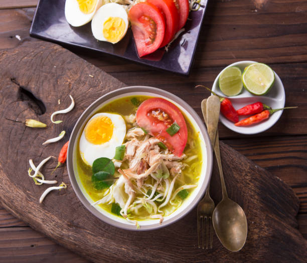 istock Soto: Indonesian chicken soup with hard boiled eggs, tomato, bean sprout, lemon, cayenne pepper on rustic brown wooden background 849604188