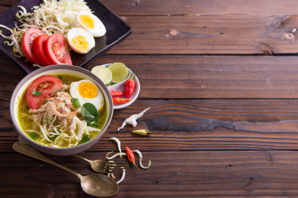 istock Soto: Indonesian chicken soup with hard boiled eggs, tomato, bean sprout, lemon, cayenne pepper on rustic brown wooden background 849604454