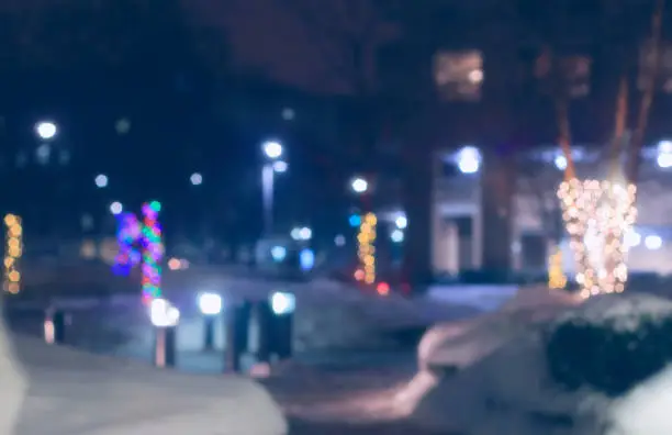 Defocused urban residential buildings with holiday lights and snow around de-iced pathway