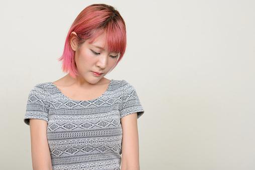 Studio shot of young beautiful Asian woman with pink hair against white background horizontal shot