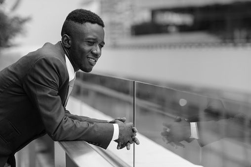 Portrait of young African businessman against view of the city in Bangkok Thailand in black and white horizontal shot