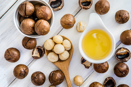 The Macadamia Nut Oil and peeled macadamia nut   on white table ,﻿use for Healthy Skin and Hair and Natural Healing Oil Treatment , overhead and top view