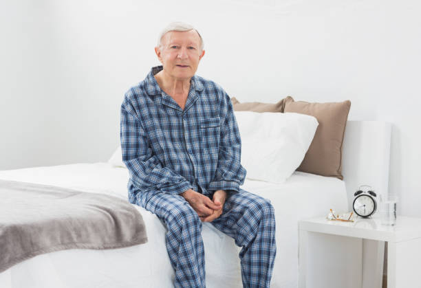 Elderly man sitting on his bed Elderly man sitting on his bed in the bedroom old man pajamas photos stock pictures, royalty-free photos & images