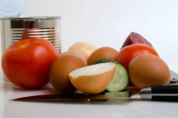 Vegetables eggs sausage knife and canned food on a light background.