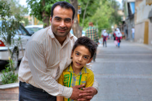 Man hugs child posing for a photographer on city street. Fars Province, Shiraz: Family portrait of father and son on a city street, man and boy posing for a photographer. iranian ethnicity stock pictures, royalty-free photos & images