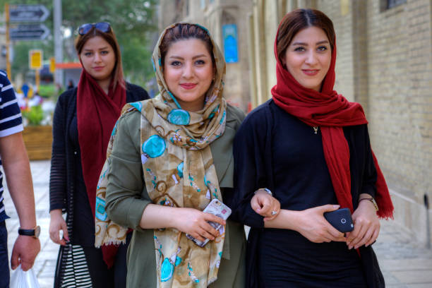 Modern young Iranian women wearing hijabs, Shiraz, Iran. Fars Province, Shiraz: Young Iranian women, dressed in hijab, are walking along a city street with smartphones in their hands. iranian ethnicity stock pictures, royalty-free photos & images