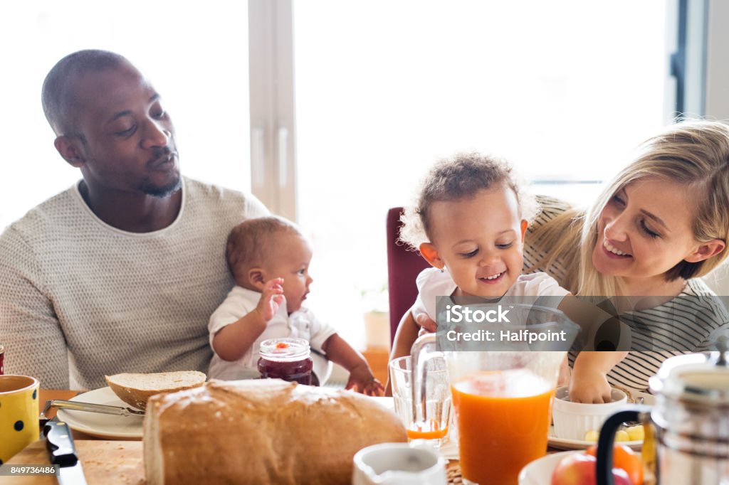 Young interracial family with little children having breakfast. Beautiful young interracial family at home with their cute daughter and little baby son having breakfast together. Family Stock Photo