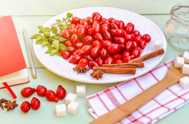 fresh red cornel berries on white plate, preparing for homemade cornelian cherry jam, surrounded by jelly jar, flax napkin, vintage spoon, sugar. - 6707 imagens e fotografias de stock