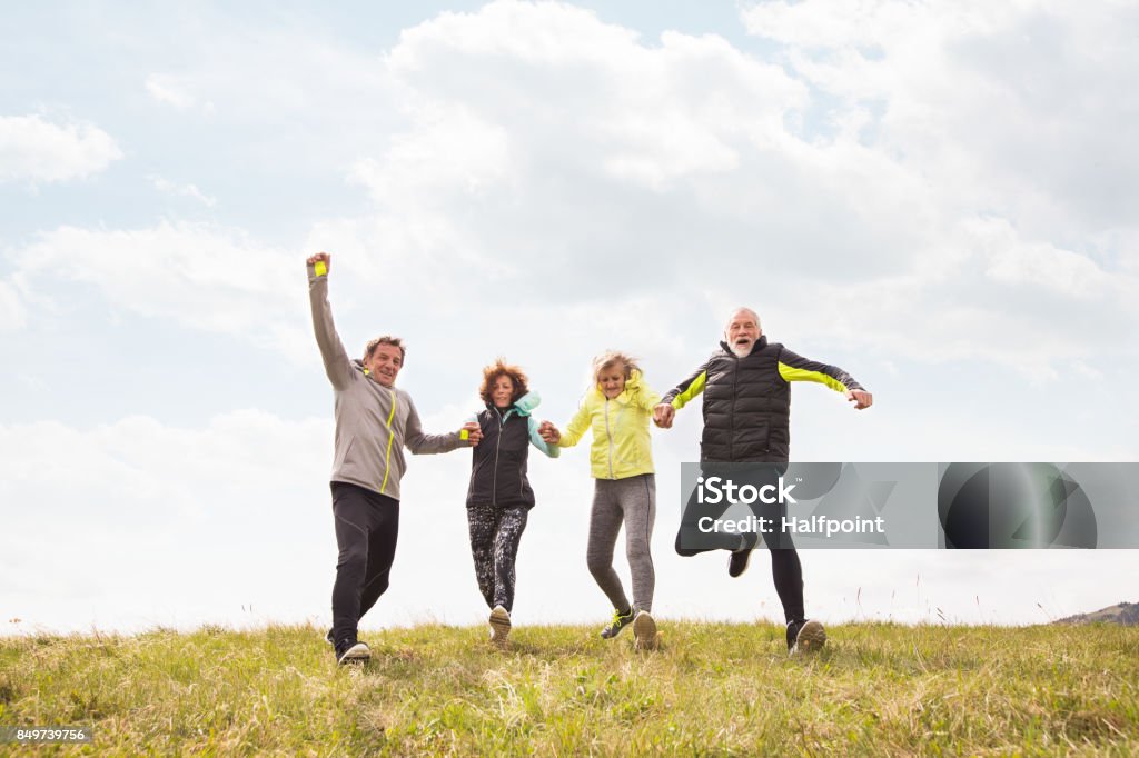 Group of senior runners outdoors, resting, holding hands. Group of active senior runners outdoors resting, holding hands, jumping and having fun. Group Of People Stock Photo