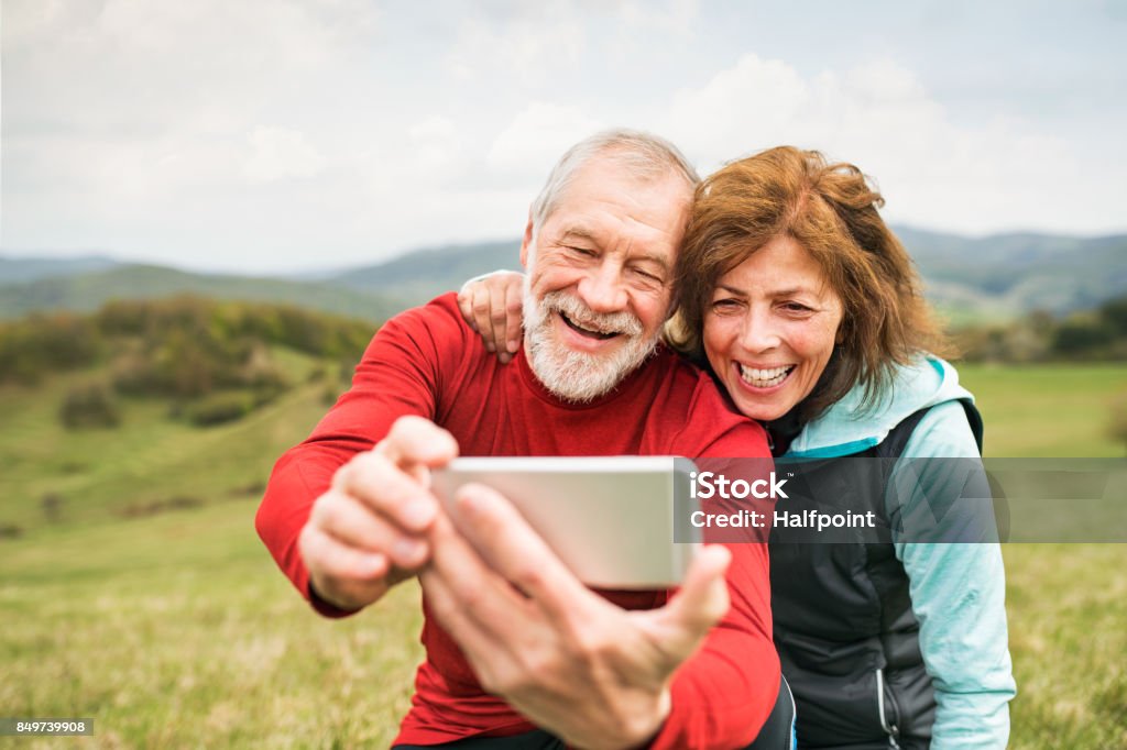 Active senior runners in nature taking photo with smart phone. Active senior runners outside on the green hills taking photo with smart phone. Calvary in Banska Stiavnica, Slovakia. Senior Adult Stock Photo