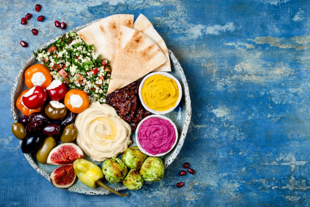 Middle Eastern meze platter with green falafel, pita, sun dried tomatoes, pumpkin and beet hummus, olives, stuffed peppers, tabbouleh, figs. Mediterranean appetizer party idea stock photo