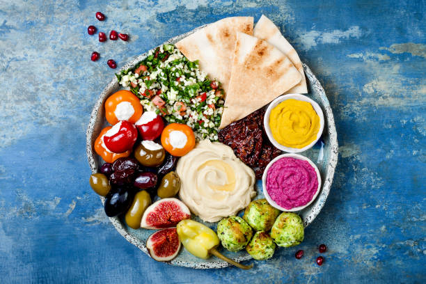 緑ファラフェル、ピタ、サンドライ トマト、カボチャ、ビートのフムス、オリーブ、ピーマン、タブレ、イチジクと中東のメゼの盛り合わせ。地中海前菜パーティーのアイデア - food platter ストックフォトと画像