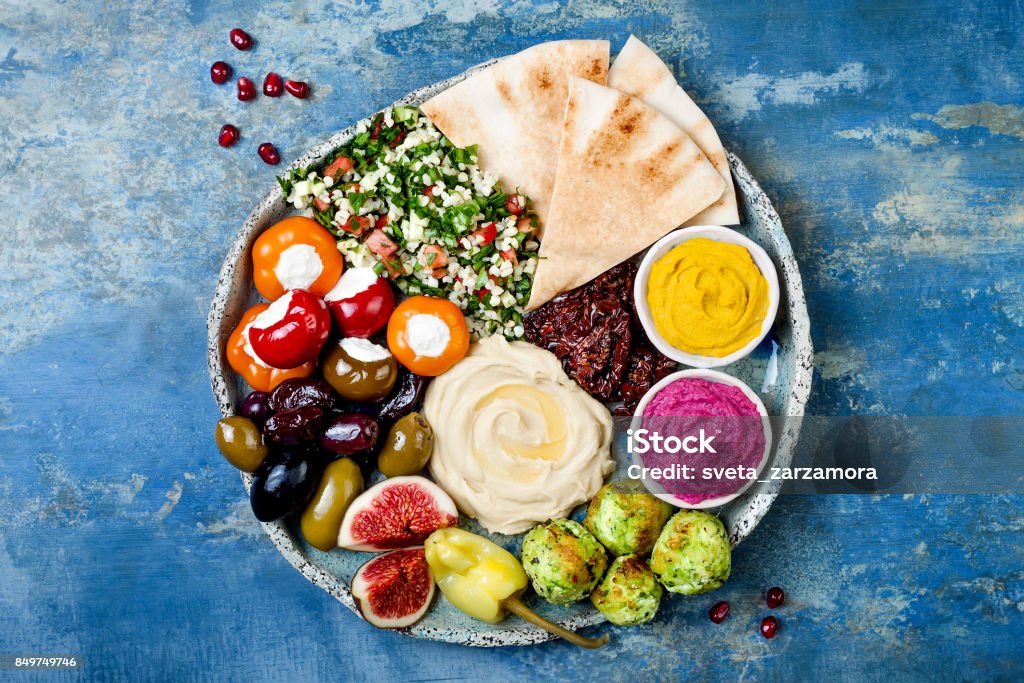 Middle Eastern meze platter with green falafel, pita, sun dried tomatoes, pumpkin and beet hummus, olives, stuffed peppers, tabbouleh, figs. Mediterranean appetizer party idea Food Stock Photo