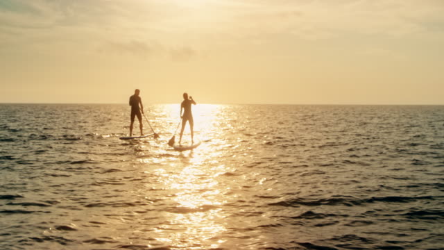 Couple standup paddling into the sunset