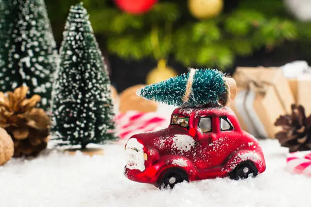 Photo of Miniature red car carrying fir tree on Christmas background