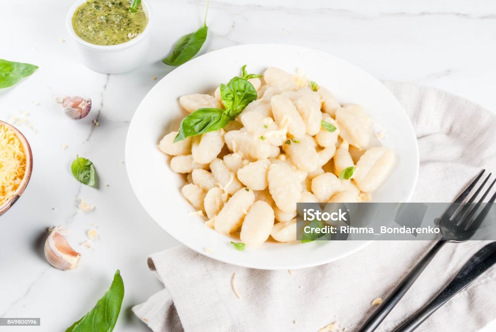 Ready to eat  potato gnocchi Italian food recipe, Healthy vegan dinner with potato gnocchi. With grated parmesan cheese, basil and pesto sauce. On white marble , copy space Above Stock Photo