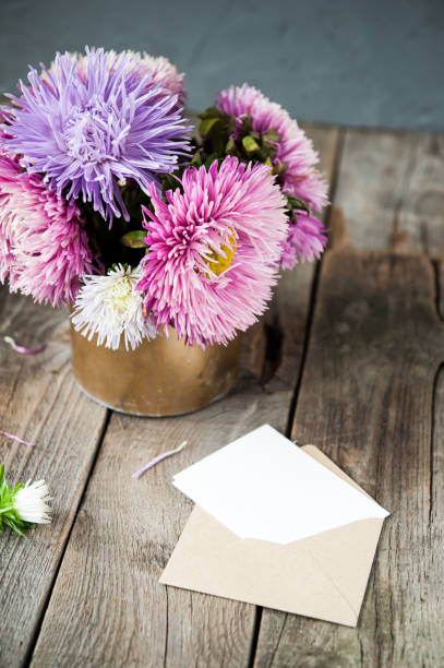 istock Multicolor aster flowers bouquet, blank white greeting card and craft paper envelope on rustic wooden table and dark grey background.. Postcard mock up. Autumn flowers. Selective focus. Space for text. 849801054