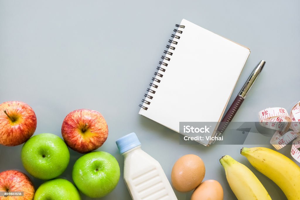 Dieting, healthy and active lifestyles Concept, apples, bananas, egges, tape measure, bottle of milk, blank notebook on grey background. top view with blank copy space Arts Culture and Entertainment Stock Photo