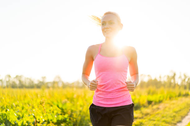 young sporty woman with blond hair jogging in rural surrounding sun flares create backlight and golden hour effect