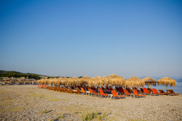 Thatched umbrellas with plastic loungers next to the coastline Sunshades made of straw, umbrellas and plastic deckchairs for a perfect holiday. thatched roof hut straw grass hut stock pictures, royalty-free photos & images