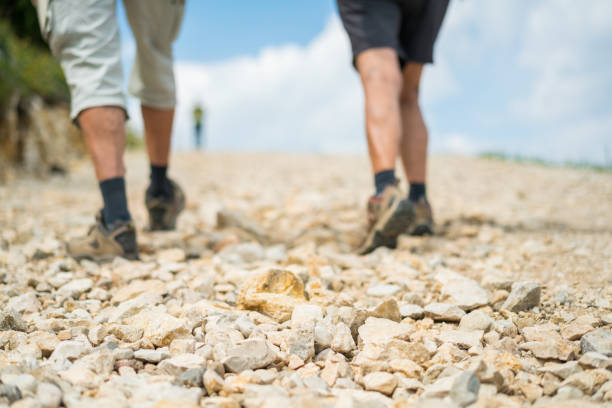 detail of senior couples legs in hiking shoes walking up stony path, focus on stones, legs blurred