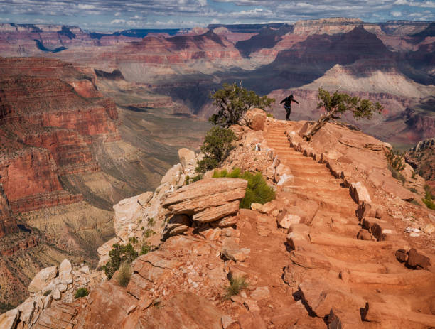 Person balances at the edge of a cliff on Cedar Ridge overlooking a deep canyon while hiking the South Kaibab Trail from the southern entrance of the Grand Canyon on a spring day, Grand Canyon National Park, Arizona, USA
