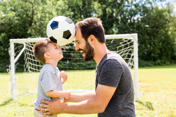 joven padre con su hijo pequeño jugando al fútbol en el campo de fútbol - canadian football fotografías e imágenes de stock