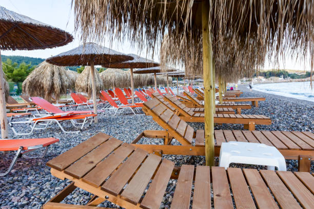 Wooden loungers with straw umbrellas for relaxing by the beach Wooden sunbed under thatched sunshades is placed on the morning beach. thatched roof hut straw grass hut stock pictures, royalty-free photos & images
