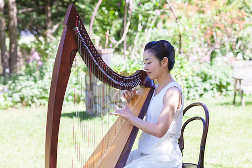 A Japanese female harpist is playing harp in a garden.