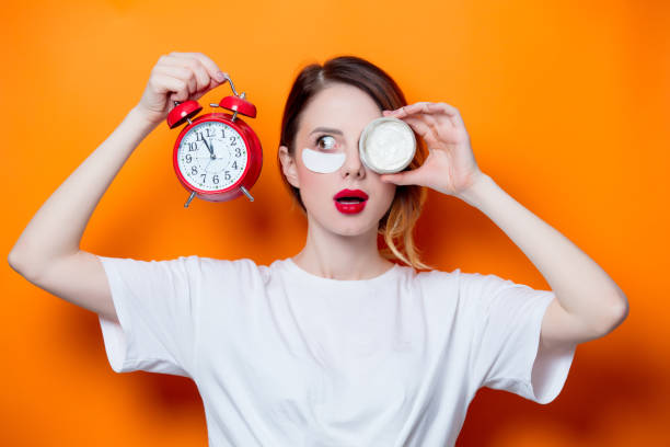 woman using eye patch for her eyes and care lips on orange background - clock face fotos imagens e fotografias de stock