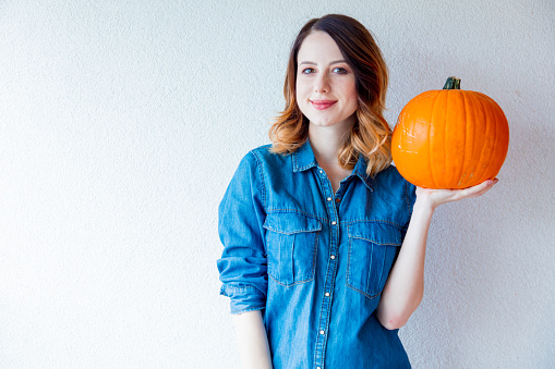 Redhead woman in jeans clothes holding orange autumn pumpkin. Portrait on white background