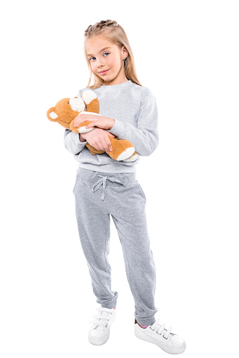 adorable little girl carrying teddy bear and looking at camera isolated on white