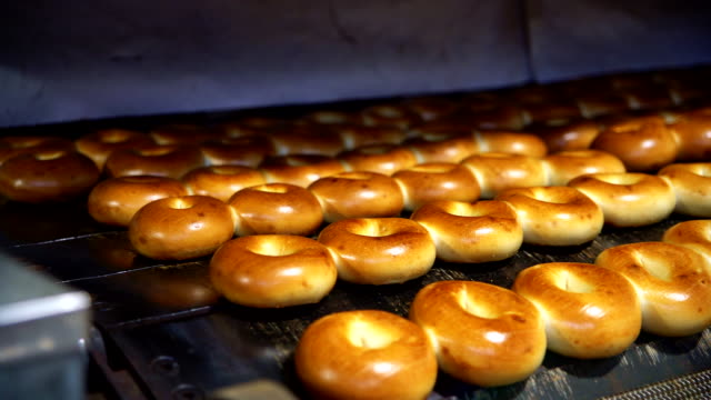 Making of the fresh hot tasty bagels at the backery's factory: plane bagels comes out from the oven. 4K UHD video with panoramic motion.