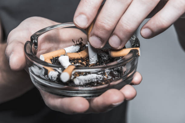 Young man ending smoking cigarette Close up of male hands extinguishing cigarette butt on glass ashtray drug addiction tattoos stock pictures, royalty-free photos & images