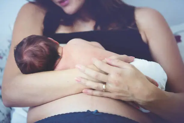 Young mother breastfeeds her baby, holding him in her arms and smiling from happiness