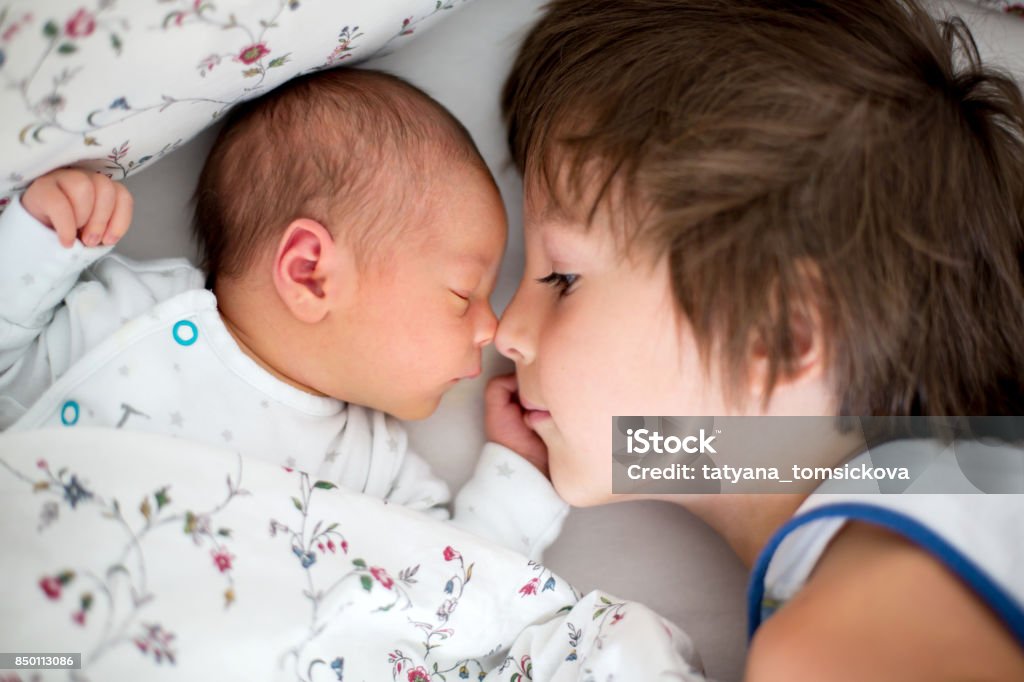 Beautiful boy, hugging with tenderness and care his newborn baby brother at home Beautiful boy, hugging with tenderness and care his newborn baby brother at home. Family love happiness concept Sibling Stock Photo
