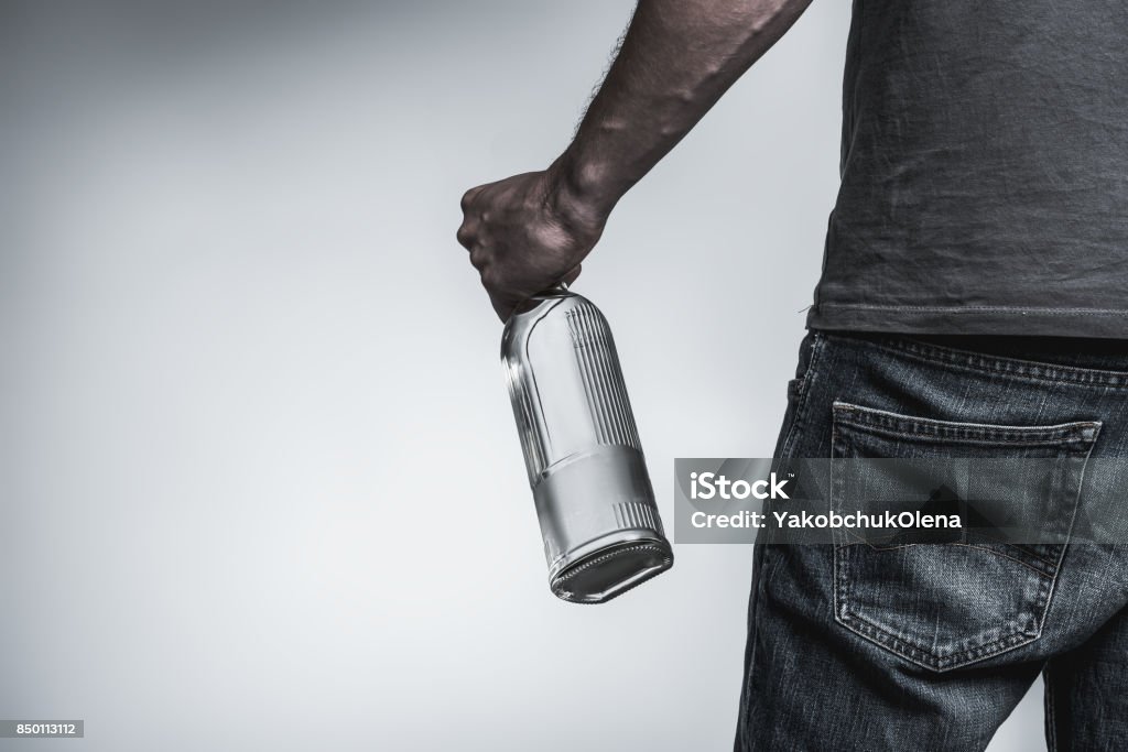Young man has alcohol addiction Close up of hand of male alcoholic holding bottle of harmful beverage. He is standing and turning back to camera. Isolated and copy space in left side Back Stock Photo