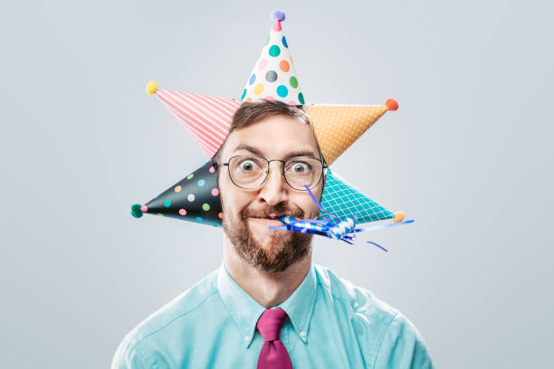 Office Worker Party Man A portrait of a man wearing business office attire sporting many birthday hats and party horn blower.  He has a crazy look on his face. bizarre fashion stock pictures, royalty-free photos & images