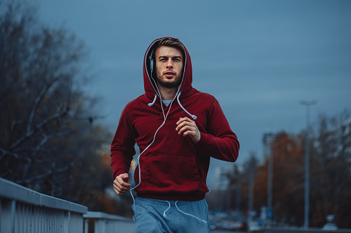 Man in red hoodie jogging beside the road in the city