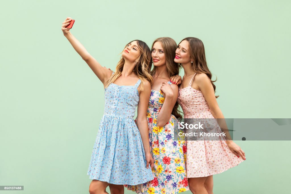 Hipsters three friends in casual dress, macking selfie on green background and have fun selfie Fashion Stock Photo