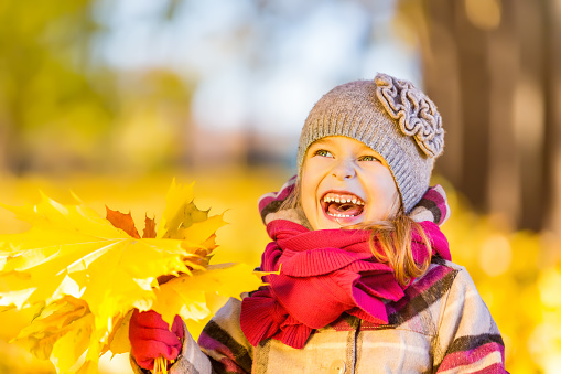 Happy little girl with autumn leaves in the park